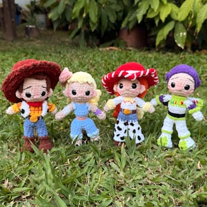Op de afbeelding: Vier handgemaakte gehaakte poppen van Toy Story-personages. De poppen zijn Woody, Bo Peep, Jessie en Buzz Lightyear, elk met hun kenmerkende outfits. Ze staan op groen gras.