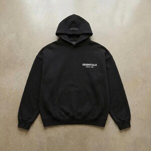 May include: Black hooded sweatshirt with a front pocket and the word "ESSENTIALS" printed in white. The sweatshirt has a drawstring hood and a small label on the hood.