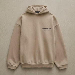 May include: A tan hoodie with a drawstring hood and long sleeves. The text "ESSENTIALS FEAR OF GOD" is printed on the upper left chest. The hoodie is made of a soft, comfortable material.