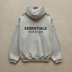 May include: A gray hoodie with the text "ESSENTIALS FEAR OF GOD" printed in black. The hoodie has a hood and a small black label at the top of the hood.
