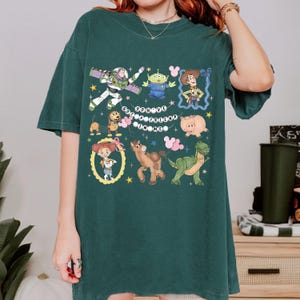 May include: Dark green t-shirt featuring colorful cartoon characters from the Toy Story movie. The shirt includes Buzz Lightyear, Woody, and other characters, with the text "You've Got a Friend in Me".