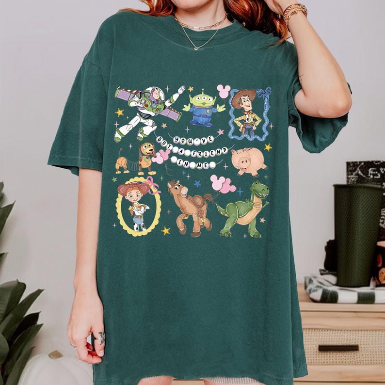 May include: Dark green t-shirt featuring colorful cartoon characters from the Toy Story movie. The shirt includes Buzz Lightyear, Woody, and other characters, with the text "You've Got a Friend in Me".