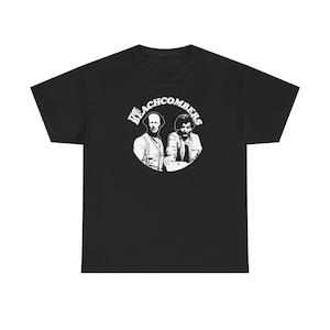 Puede incluir: Camiseta negra con un gráfico blanco de dos hombres y el texto "THE BEACHCOMBERS" en un diseño circular. El gráfico es una ilustración en blanco y negro. La camiseta está hecha de un material suave y cómodo.