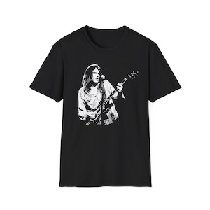 May include: Black t-shirt featuring a white graphic of a musician playing a guitar. The graphic is a detailed illustration of a person with long hair, wearing a plaid shirt, and playing an electric guitar. The shirt is a classic crew neck style.