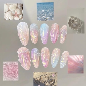 Op de afbeelding: Een verzameling iriserende, gebeeldhouwde nagelkunst in verschillende tinten roze, paars en blauw, versierd met parelaccenten. Het ontwerp roept een zeemeermin- of oceaanthema op, met een zeeschelp en zeester op de achtergrond.