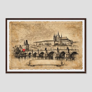 May include: A framed vintage-style map print featuring a detailed black ink illustration of the Charles Bridge and Prague Castle. A small, solid red heart icon is positioned near the bridge tower, and a blank decorative scroll banner sits below.