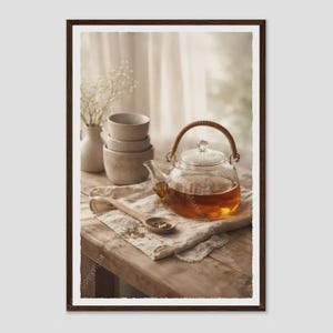 May include: A clear glass teapot with a woven handle filled with amber tea, sitting on a beige linen cloth next to a wooden spoon, a stack of two speckled ceramic bowls, and a small vase containing white baby's breath flowers.