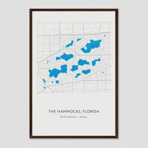 May include: A framed map print of The Hammocks, Florida, featuring a white background with grey street grid lines and bright blue shapes representing bodies of water. The text reads THE HAMMOCKS, FLORIDA and WEST KENDALL / MIAMI.