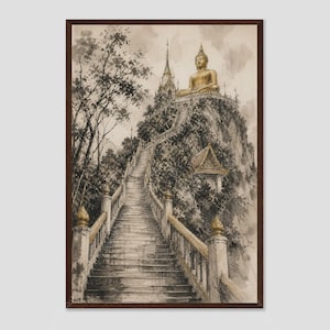 Op de afbeelding: Een ingelijste wandkunstprint met een aquarelillustratie van een lange stenen trap die een steile, met bomen begroeide berg op leidt naar een gouden Boeddhabeeld bovenop een tempelstructuur onder een bewolkte, gedempte lucht.
