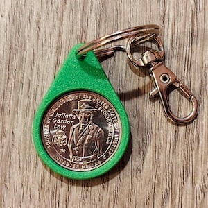May include: A green teardrop-shaped keychain with a silver coin featuring Juliette Gordon Low, founder of the Girl Scouts, and the text "Quarter Dollar". The keychain has a silver clasp and ring.