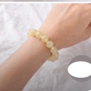 May include: A bracelet composed of smooth, round, pale yellow beads with a translucent finish. The beads are uniform in size and strung together in a circular shape, creating a simple and continuous design that rests comfortably on the wrist.