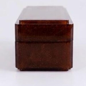 May include: A rectangular box with a deep amber, translucent finish and a subtle glittery texture. The object features a stepped lid design with sharp, clean edges and a smooth, polished surface, presented from a front-facing perspective.