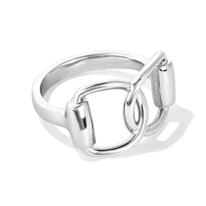 May include: A silver-colored ring with a horse bit design. The ring features a rounded band and a detailed bit, showcasing a classic equestrian theme. The ring is made of a shiny, reflective metal.
