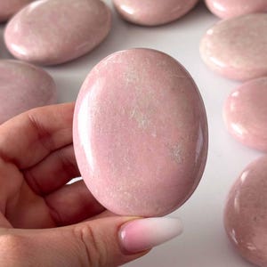 Peut inclure: Plusieurs pierres roses lisses de forme ovale. Les pierres ont une surface polie et varient légèrement de teinte. L'image montre plusieurs pierres, dont une tenue dans une main, soulignant leur couleur et leur texture naturelles. Ces pierres sont idéales pour la méditation ou la décoration.