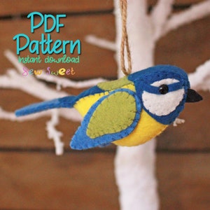 Op de afbeelding: PDF-patroon voor een blauwe vogel ornament. De vogel is gemaakt van vilt en heeft een geel lichaam, blauwe vleugels en een witte borst. Het patroon is beschikbaar voor directe download. De tekst "Sew Sweet" is ook zichtbaar in de afbeelding.