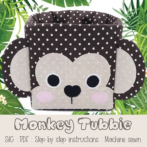 Puede incluir: Un contenedor de almacenamiento de tela con lunares marrones y blancos con forma de cara de mono. El contenedor tiene una cara beige con ojos negros, una nariz negra y mejillas rosadas. El texto "Monkey Tubbie" está escrito debajo del contenedor. El texto "SVG : PDF : Step by step instructions : Machine sewn" está escrito debajo del texto "Monkey Tubbie".