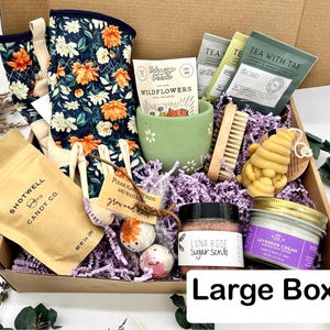 May include: A large gift box filled with gardening and self-care items. Includes floral gardening gloves, wildflower seeds, tea packets, a green ceramic cup, a wooden brush, a bee-shaped soap, sugar scrub, lavender cream, and candy. The box is labeled "Large Box".