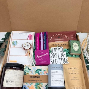 Puede incluir: Una caja de regalo con un bloc de notas, una piruleta, tres bol&iacute;grafos de gel, una barrita de cereales, una caja verde, una pegatina que dice I READ PAST MY BED TIME, una vela Hidden Library, un marcap&aacute;ginas de tela floral, t&eacute; y caramelos.