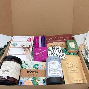 Puede incluir: Una caja de regalo de cart&oacute;n que contiene una vela Hidden Library, un marcap&aacute;ginas floral, un bloc de notas, tres bol&iacute;grafos de gel, una barrita de cereales Chocolate Hour, una cajita con forma de libro, t&eacute;, caramelos y una piruleta.