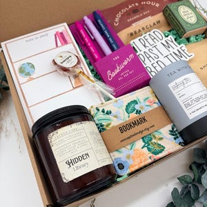 Puede incluir: Una caja de regalo que contiene una vela de soja Hidden Library, un marcap&aacute;ginas de tela floral, una lata de t&eacute; gris, un bloc de notas con la etiqueta note to shelf, tres bol&iacute;grafos de gel, una barrita de granola de chocolate y una piruleta.