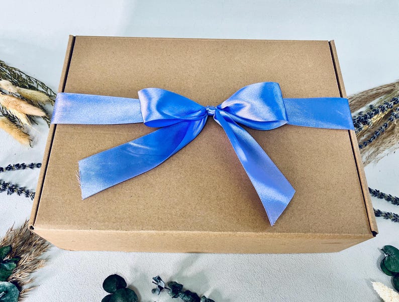May include: A brown cardboard gift box tied with a light blue satin ribbon and bow. The box is rectangular and closed. The ribbon is wrapped around the box and tied in a bow on top.