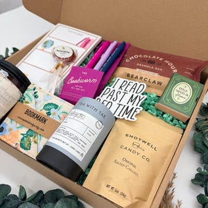 Puede incluir: Una caja de regalo que contiene un bote de t&eacute; Tea With Tae, una bolsa de caramelo salado Shotwell Candy Co., una barrita de granola Chocolate Hour, un set de bol&iacute;grafos de gel Bookworm, un marcap&aacute;ginas floral, una piruleta, una caja verde Once Upon a Flame y una pegatina con el texto I READ PAST MY BED TIME.