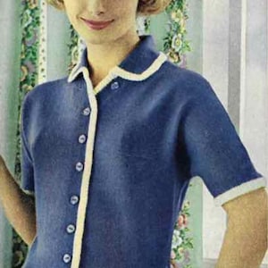 Puede incluir: Una blusa de punto azul de estilo vintage con mangas cortas, cuello blanco y cierre de botones. La blusa tiene ribetes blancos en el cuello y las mangas. La mujer lleva una pulsera dorada. El fondo presenta una cortina floral.