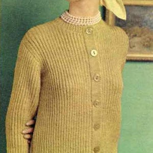 May include: A woman wearing a mustard yellow knit cardigan with matching skirt. The cardigan has button closures and long sleeves. She is also wearing a pearl necklace and a matching headscarf.