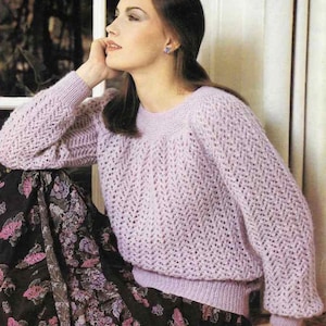 May include: A light purple knitted sweater with a textured pattern. The sweater has long sleeves and a ribbed hem and cuffs. The model is wearing a floral skirt. The sweater is a classic style.