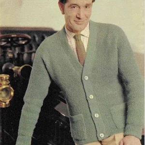 May include: A light green cardigan sweater with a ribbed knit texture, button closure, and two front pockets. The sweater is worn over a collared shirt and tie. The man is leaning on a black object.