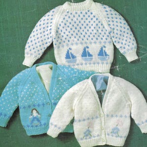 Könnte beinhalten: Drei gestrickte Pullover und Strickjacken in Weiß und Blau. Einer ist ein Rundhalspullover mit blauen Segelboot- und Herzmustern. Die anderen beiden sind Strickjacken, eine hellblaue mit einem Mädchenmuster und die andere weiße mit floralen Details.
