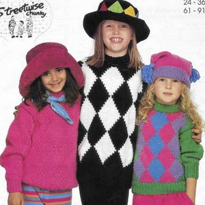 Puede incluir: Tres niños con jerséis y sombreros de punto. Los jerséis presentan patrones de rombos y argyle en varios colores, incluyendo rosa, negro, blanco, verde y azul. Un niño lleva un sombrero negro con formas geométricas coloridas.