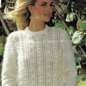 Puede incluir: Suéter de color crema de manga larga con un patrón de punto texturizado. El suéter presenta rayas verticales y pequeñas bolitas en relieve. El cuello es redondo. La modelo lleva pendientes y tiene el pelo rubio.