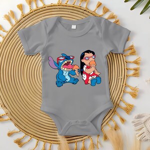 May include: Gray baby onesie featuring a colorful graphic of Stitch and Lilo from the Disney movie Lilo & Stitch. Stitch is blue, wearing sunglasses, and eating ice cream. Lilo is wearing a red dress and eating ice cream.