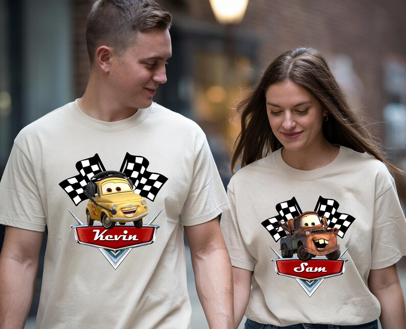 May include: Beige t-shirts featuring cartoon car graphics with checkered flags. One shirt has a yellow car with the name "Kevin" on a red banner. The other shirt has a brown car with the name "Sam".