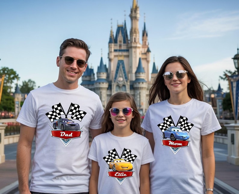 May include: Three people wearing white t-shirts with car graphics and text. The shirts feature a checkered flag design and the words "Dad", "Mom", and "Ellie" on red banners. The background includes a castle.