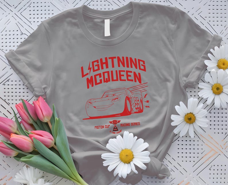 May include: A gray t-shirt featuring the text "LIGHTNING MCQUEEN" in red, along with a red graphic of a race car. The shirt also includes the text "Piston Cup Racing Series".