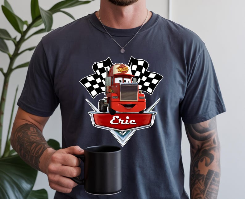 May include: Dark gray t-shirt featuring a red cartoon truck with the name "Eric" on a shield. The truck has a smiling face and is flanked by two checkered flags. The word "Rusteze" is on the truck's roof.