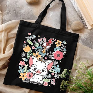 Może przedstawiać: Czarna torba typu tote z kolorową grafiką przedstawiającą świnię, koguta i elementy kwiatowe. Projekt zawiera r&oacute;żowe, ż&oacute;łte, niebieskie i zielone kwiaty. Torba ma czarne uchwyty i jest prawdopodobnie wykonana z pł&oacute;tna lub podobnego materiału.