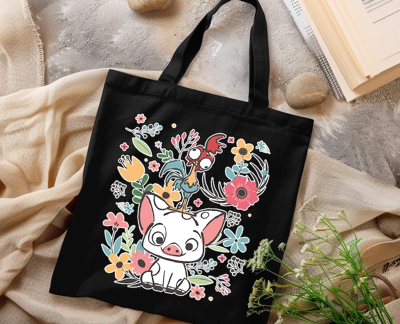 Może przedstawiać: Czarna torba typu tote z kolorową grafiką przedstawiającą świnię, koguta i elementy kwiatowe. Projekt zawiera r&oacute;żowe, ż&oacute;łte, niebieskie i zielone kwiaty. Torba ma czarne uchwyty i jest prawdopodobnie wykonana z pł&oacute;tna lub podobnego materiału.