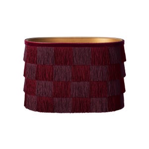 May include: A cylindrical lampshade with a tiered fringe design in shades of burgundy and maroon. The top edge is trimmed with a dark red velvet band, and the interior has a gold finish. This decorative lampshade adds a touch of elegance.