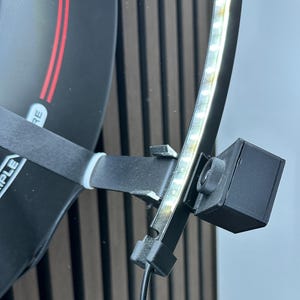 Puede incluir: Un dispositivo negro con una tira de luz y una peque&ntilde;a caja negra adjunta. La tira de luz tiene varias luces blancas peque&ntilde;as. El dispositivo est&aacute; montado en un objeto negro con detalles en rojo y la palabra "RE" visible.