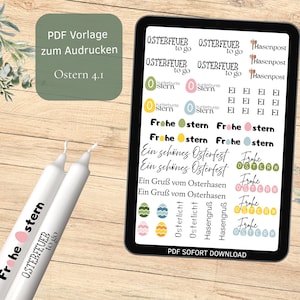 Könnte beinhalten: Ein Tablet-PC zeigt Ostermotive und Texte, darunter "Frohe Ostern" und "Osterfeuer to go". Zwei weiße Kerzen mit ähnlichem Text befinden sich im Vordergrund. Der Hintergrund ist eine helle Holzoberfläche mit floralen Akzenten.