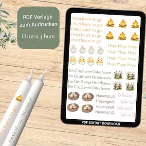 Könnte beinhalten: Ein digitales Tablet zeigt Grafiken zum Thema Ostern, darunter Hasen, Küken und Text. Im Vordergrund befinden sich zwei weiße Kerzen mit Ostermotiven und Text. Der Text enthält "Osterfeuer to go" und "Ein Gruß vom Osterhasen."