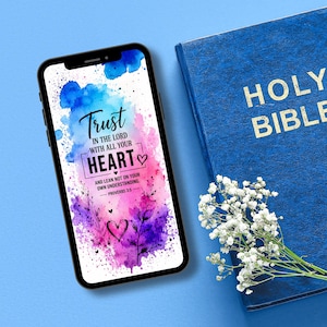 Könnte beinhalten: Ein Smartphone zeigt ein Aquarelldesign mit dem Text "Vertraue dem Herrn von ganzem Herzen". Eine blaue Bibel mit goldener Schrift und ein Strauß weißer Blumen sind ebenfalls im Bild.