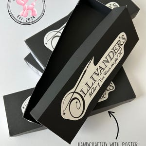 May include: Black rectangular boxes with the text "LLIVANDER'S Makers of Fine Wands since 382 BC" in white. The boxes are stacked, with one open to reveal the interior. The text "HANDCRAFTED WITH POSTER BOARD MATERIAL" is also visible.
