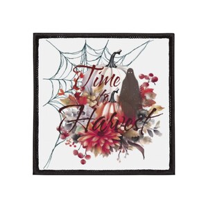 Puede incluir: Parche cuadrado con borde negro con un diseño de Halloween. Una calabaza blanca y una calabaza naranja más pequeña están rodeadas de follaje otoñal, bayas y un fantasma negro. Las palabras "Time for Harvest" están escritas en una fuente cursiva.