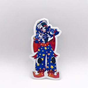 Puede incluir: Una pegatina con un personaje de dibujos animados con un atuendo azul adornado con estrellas amarillas. El personaje tiene una cara blanca y negra, ojos rojos y un sombrero con estampado azul y blanco. Los lazos rojos y los zapatos naranjas completan el diseño.