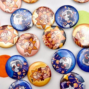May include: A collection of colorful, round pinback buttons. The buttons feature various cartoon character designs with a sun and moon theme. The buttons are in shades of blue, yellow, orange, and pink.