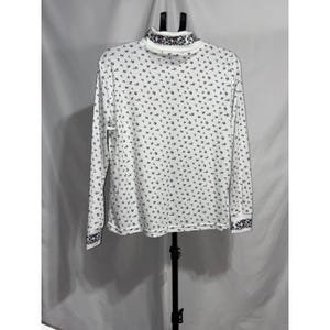 May include: A white long-sleeve shirt featuring a small black floral pattern across the body. The garment includes a mock neck collar and sleeve cuffs, both decorated with a distinct, larger floral print in shades of red, green, and black.